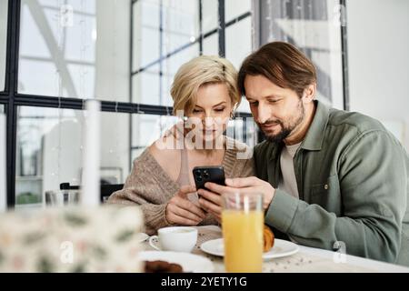 Una coppia si siede a casa, condividendo risate e calore durante la colazione e uno smartphone. Foto Stock