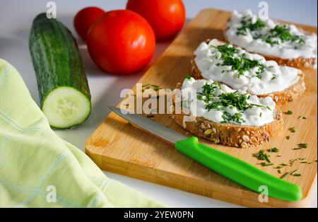 Primo piano di tre fette di pane integrale spalmato con burro e formaggio fresco cosparso di erba cipollina appena tritata su un tagliere di bambù Foto Stock