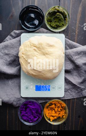 Impasto di pane su una bilancia da cucina con colorazioni naturali: Preparazione di pane al latte multicolore con curcuma, matcha, carbone e patate dolci viola Foto Stock