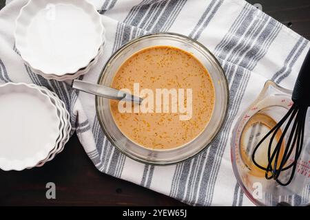 Tuorli d'uovo mescolati nel latte riscaldato infuso con il caffè: Frammenti di tuorli d'uovo che galleggiano in un composto di caffè e latte in un recipiente di miscelazione in vetro Foto Stock