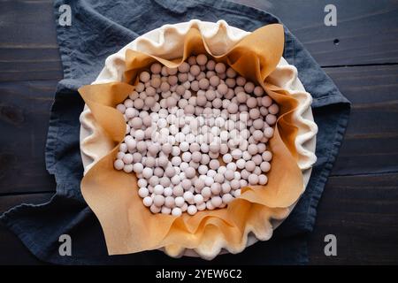 Preparazione per cuocere ciecamente una crosta scanalata: Crosta per torte rivestita con carta pergamena e riempita con pesi per torte in ceramica per cuocere alla cieca Foto Stock