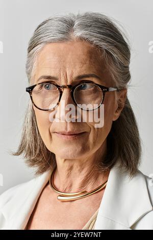 Una donna matura con bellissimi capelli grigi sfoggia la sua eleganza in un elegante abito bianco e occhiali. Foto Stock