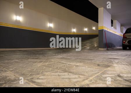 Un'area parcheggio sotterranea vuota con pavimenti piastrellati e illuminazione soffusa. Le strisce gialle aggiungono un tocco moderno, enfatizzando l'ambiente pulito e strutturato Foto Stock