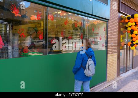 Una donna guarda fuori dalla finestra di un negozio con uno sfondo verde. Il negozio ha un tema di Halloween, con decorazioni rosse e nere sulle finestre Foto Stock