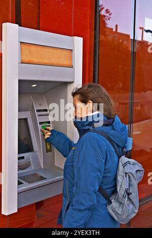 Una donna sta usando un lettore di carte per pagare qualcosa. Indossa una giacca blu e uno zaino Foto Stock