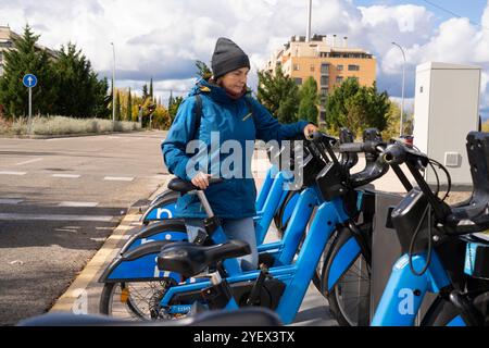 Una donna con una giacca blu si trova accanto a una bici blu. La bici è parcheggiata accanto a molte altre biciclette Foto Stock