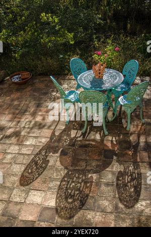 Mobili da giardino metallizzati che gettano ombre su una terrazza piastrellata di argilla, al tramonto, in un giardino sulle montagne andine orientali della Colombia centrale. Foto Stock