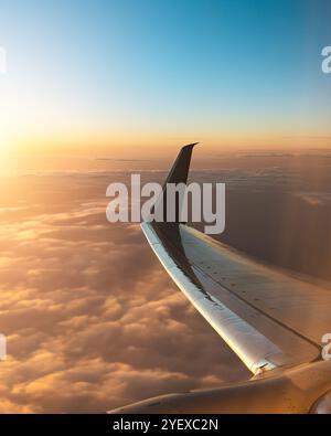 Vista dalla finestra di un aeroplano che mostra l'Ala sullo sfondo di Un tramonto dorato e nuvole soffici, catturando la bellezza del viaggio aereo e del Sere Foto Stock