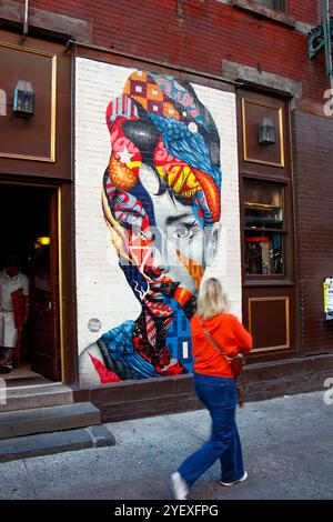 Colorato murale di audrey hepburn su un muro di mattoni in via dei gelsi, Little italy New york, persone che camminano in primo piano e un idrante del fuoco Foto Stock