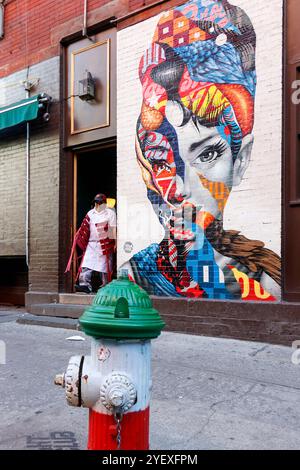 Colorato murale di audrey hepburn su un muro di mattoni in via dei gelsi, Little italy New york, persone che camminano in primo piano e un idrante del fuoco Foto Stock