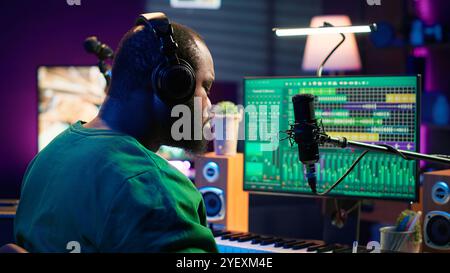 Un famoso compositore di talento scrive nuovi versi e testi in studio, componendo musica con software digitale. L'artista cantautore lavora con apparecchiature audio e attrezzature, registrando tracce. Telecamera A.. Foto Stock