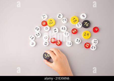 Mani dei bambini che sistemano tappi per bottiglie in plastica con numeri scritti a mano e dati moltiplicati su sfondo grigio. Attività didattica di matematica per ki Foto Stock