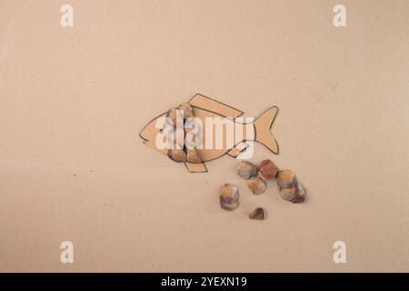 processo di realizzazione di un'imbarcazione a forma di pesce utilizzando scaglie di semi di coni di pino e cartone su sfondo beige. Progetto ispirato alla natura fai da te per l'istruzione Foto Stock