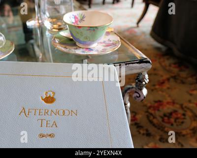 Menu bianco con copertina rigida per il tè pomeridiano con tavolini sullo sfondo per il tè tradizionale e dolci e salati pomeridiani; lettere in rilievo oro. Foto Stock