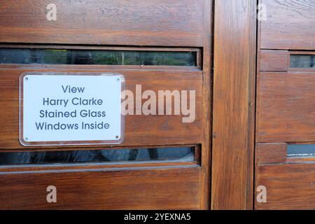 Cartello sulla porta della chiesa di Santa Maria del Rosario, per informare i visitatori della vetrata di Harry Clarke all'interno; Cong, Co Mayo, Irlanda. Foto Stock