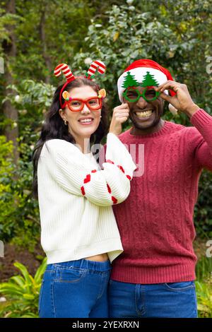 Felice coppia multirazziale che indossa occhiali e maglioni per festeggiare il Natale all'aperto Foto Stock