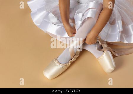 Piccola ballerina che lega scarpe pointe su sfondo beige, primo piano Foto Stock