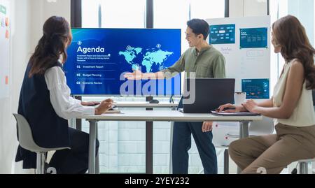leader asiatico che presenta dati e strategie finanziari in un ufficio moderno con grafici e grafici visualizzati su un grande schermo Foto Stock