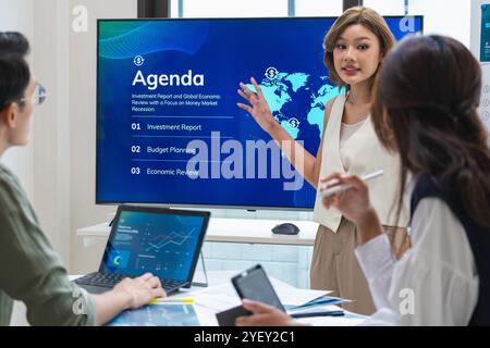 leader asiatico che presenta dati e strategie finanziari in un ufficio moderno con grafici e grafici visualizzati su un grande schermo Foto Stock