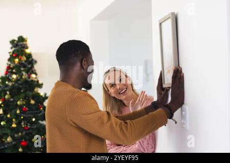 coppia multirazziale appesa foto vicino all'albero di natale, a casa Foto Stock