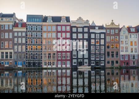 Le foglie d'oro fluttuano sopra gli iconici e stretti edifici che costeggiano i canali di Amsterdam, creando una pittoresca vista autunnale. Le calme acque rispecchiano la loro bellezza mentre il crepuscolo inizia a stabilirsi. Foto Stock