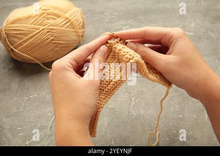 Mani femminili in maglia. Filati a maglia beige su sfondo grigio. Vista dall'alto Foto Stock