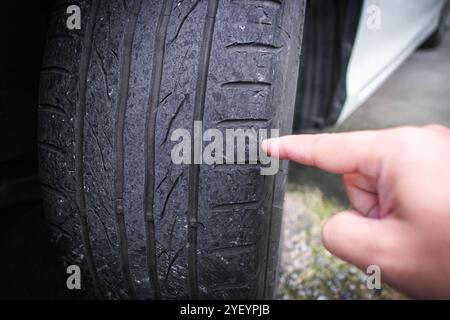 Una mano che indica l'usura del battistrada di un'auto, un primo piano del deterioramento del battistrada dell'auto dall'uso, concetto di manutenzione dell'auto Foto Stock
