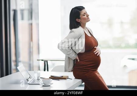 Mal di stomaco, donna incinta e d'affari in ufficio, scrivania e scomoda con mal di schiena, nausea e malattie. Pensare, preoccuparsi e aspettare aiuto Foto Stock