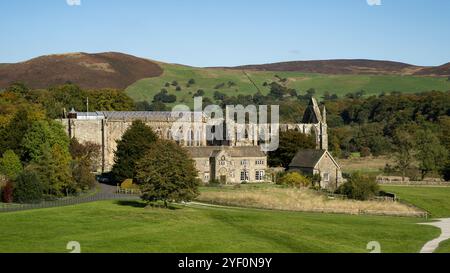 Vista panoramica della campagna sulle pittoresche rovine monastiche illuminate dal sole dell'abbazia di Bolton, la chiesa del Priorato, l'Old Rectory e le colline ondulate) - Yorkshire Dales, Inghilterra, Regno Unito. Foto Stock