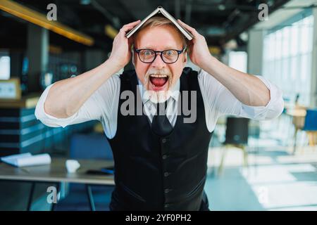 Vecchio emotivo in occhiali con un taccuino in ufficio. Un vecchio uomo d'affari si aggrava sulla fronte. Foto Stock