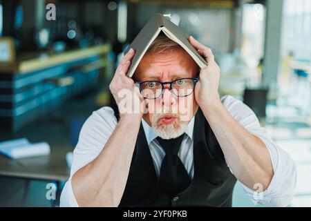 Vecchio emotivo in occhiali con un taccuino in ufficio. Un vecchio uomo d'affari si aggrava sulla fronte. Foto Stock