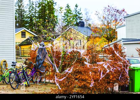 Casa cittadina decorata da Halloween con figure di scheletro tra foglie autunnali, biciclette e finte ragnatele nel cortile anteriore. Foto Stock