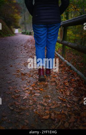 Donna con stivali rossi che cammina nel bosco con le foglie Foto Stock