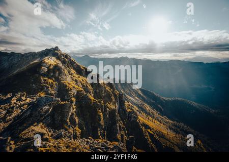 Il sole luminoso splende magnificamente attraverso le soffici nuvole che fluttuano sulle maestose montagne in lontananza Foto Stock