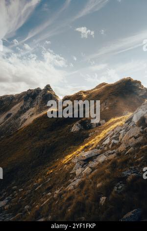 Il sole luminoso splende magnificamente attraverso le soffici nuvole che sorvolano le maestose montagne in lontananza Foto Stock