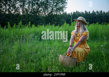 Una donna vestita con uno splendido abito giallo si trova graziosamente in un lussureggiante campo verde Foto Stock