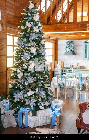 L'albero di Natale e' decorato con ornamenti e archi blu e bianco, circondato da regali sul soggiorno e sullo sfondo della cucina. Le confezioni regalo sono confezionate Foto Stock