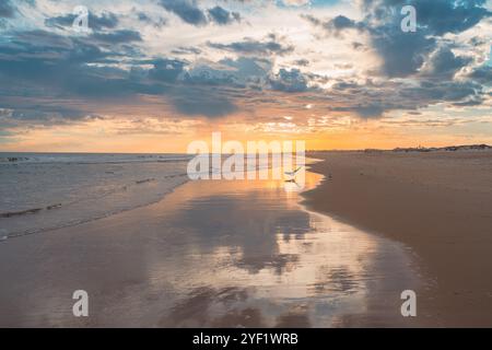 I riflessi di nuvole spettacolari e i vibranti colori del tramonto si estendono lungo la costa. Foto Stock