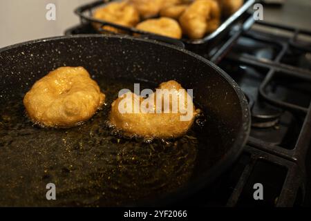 Primo piano di ciambelle sufganiyot dorate che friggono in olio caldo su un piano cottura, un tradizionale regalo Hanukkah. Le ciambelle vengono successivamente cosparse di zucchero, evidenziandone la consistenza croccante. Foto Stock