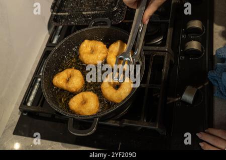 Primo piano di ciambelle sufganiyot dorate che friggono in olio caldo su un piano cottura, un tradizionale regalo Hanukkah. Le ciambelle vengono successivamente cosparse di zucchero, evidenziandone la consistenza croccante. Foto Stock