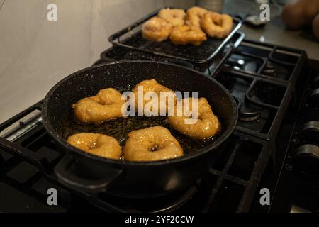 Primo piano di ciambelle sufganiyot dorate che friggono in olio caldo su un piano cottura, un tradizionale regalo Hanukkah. Le ciambelle vengono successivamente cosparse di zucchero, evidenziandone la consistenza croccante. Foto Stock