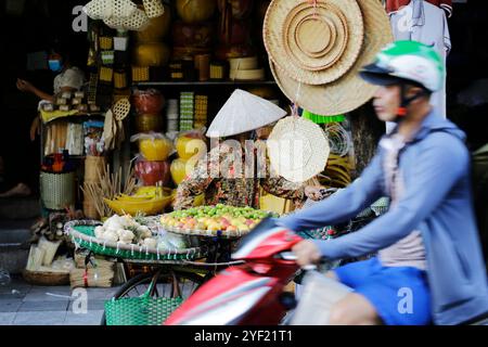 Hanoi, Vietnam - 14 luglio 2023: Donna vietnamita, che indossa il tradizionale cappello conico noto come non la, vende frutta e verdura. Foto Stock