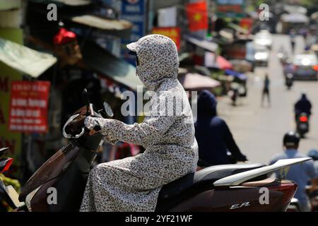 Hanoi, Vietnam - 2 luglio 2023: Una donna indossa abiti per proteggersi dal sole caldo estremo mentre percorre una strada durante una forte ondata di caldo. Foto Stock