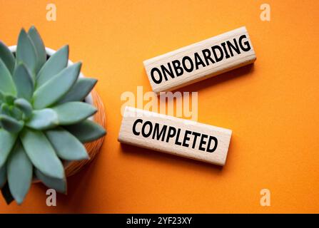 Simbolo onboarding completato. Termine concettuale onboarding completato su blocchi di legno. Bellissimo sfondo arancione con piante succulente. Affari e Onboar Foto Stock