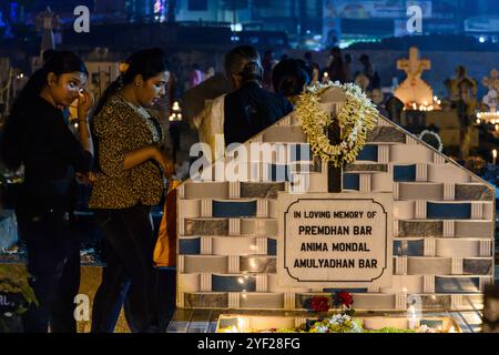 Due ragazze passano davanti a un cimitero mentre i cattolici indiani pregano per i loro parenti defunti durante la commemorazione del giorno dell'All Souls in un cimitero. I cattolici indiani accendono le candele e pregano per i loro familiari defunti in questo giorno. Foto Stock