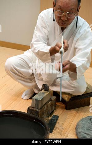 Uomo che affila una breve spada giapponese chiamata "wakizashi" in modo tradizionale con una pietra affilante a Seki City, Gifu, Giappone. Foto Stock