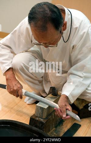 Uomo che affila una breve spada giapponese chiamata "wakizashi" in modo tradizionale con una pietra affilante a Seki City, Gifu, Giappone. Foto Stock