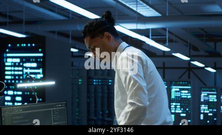 Informatico del data center responsabile dell'installazione di apparecchiature di rete per la risoluzione delle attività. Uomo indiano al lavoro che fa manutenzione sull'infrastruttura della sala server, telecamera A Foto Stock