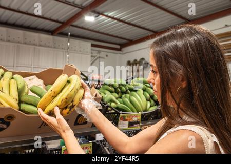 Una donna sta guardando un mucchio di banane in un negozio. Sta tenendo un mucchio di banane in mano Foto Stock