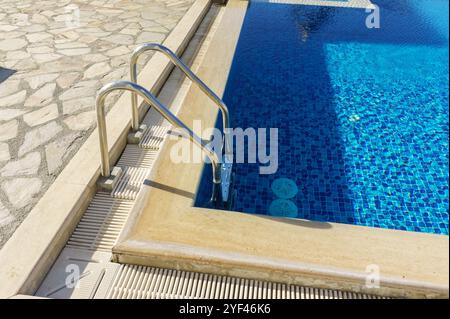 Le scale conducono a scintillanti acque blu, invitanti momenti di relax e svago in un'atmosfera soleggiata vicino alla piscina. Foto Stock